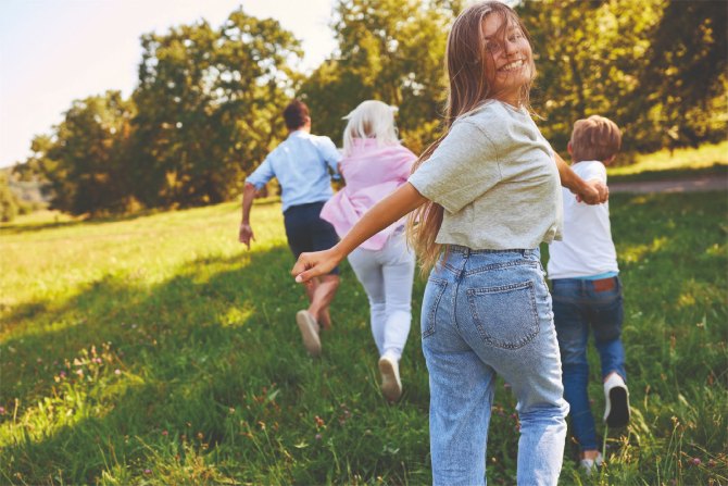 Fröhliches Mädchen läuft über Wiese gemeinsam mit anderen Kindern